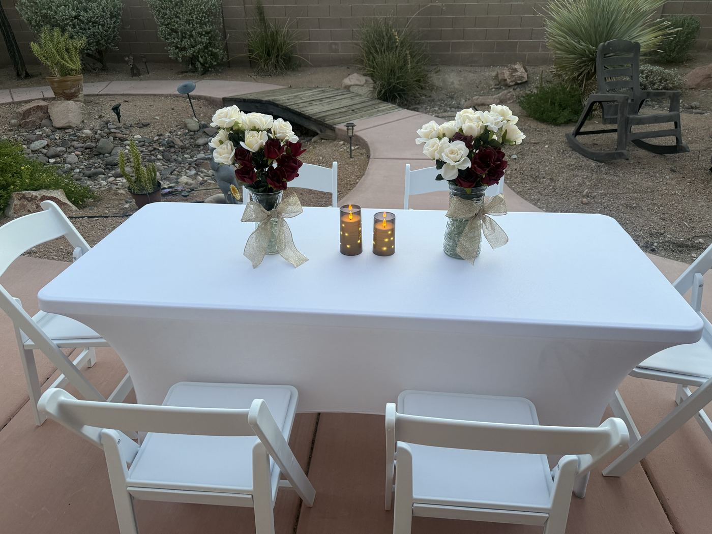 Sweetheart table with rose arrangements and candles set up in a backyard