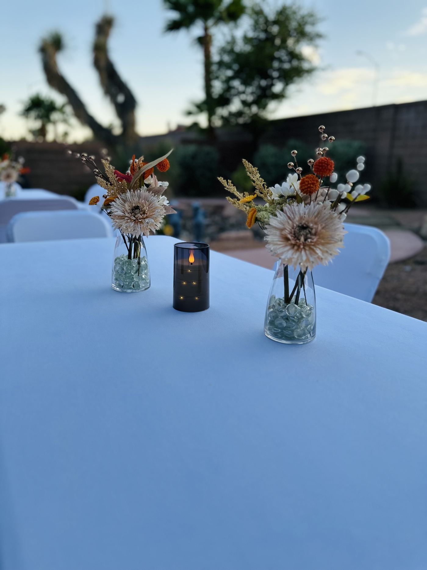 Bud vases and a flameless candle on a white linen table at dusk