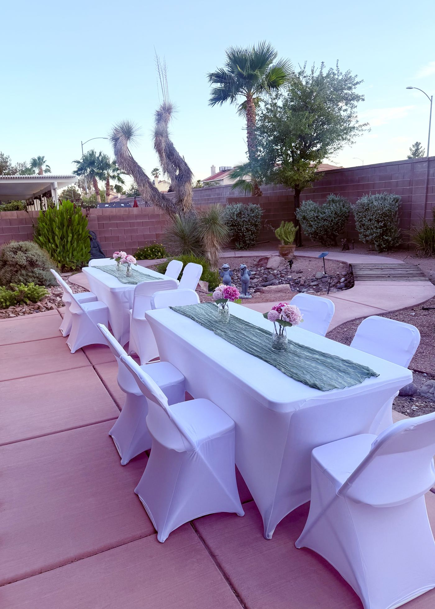 Two banquet tables with sage runners and white chair covers on a patio