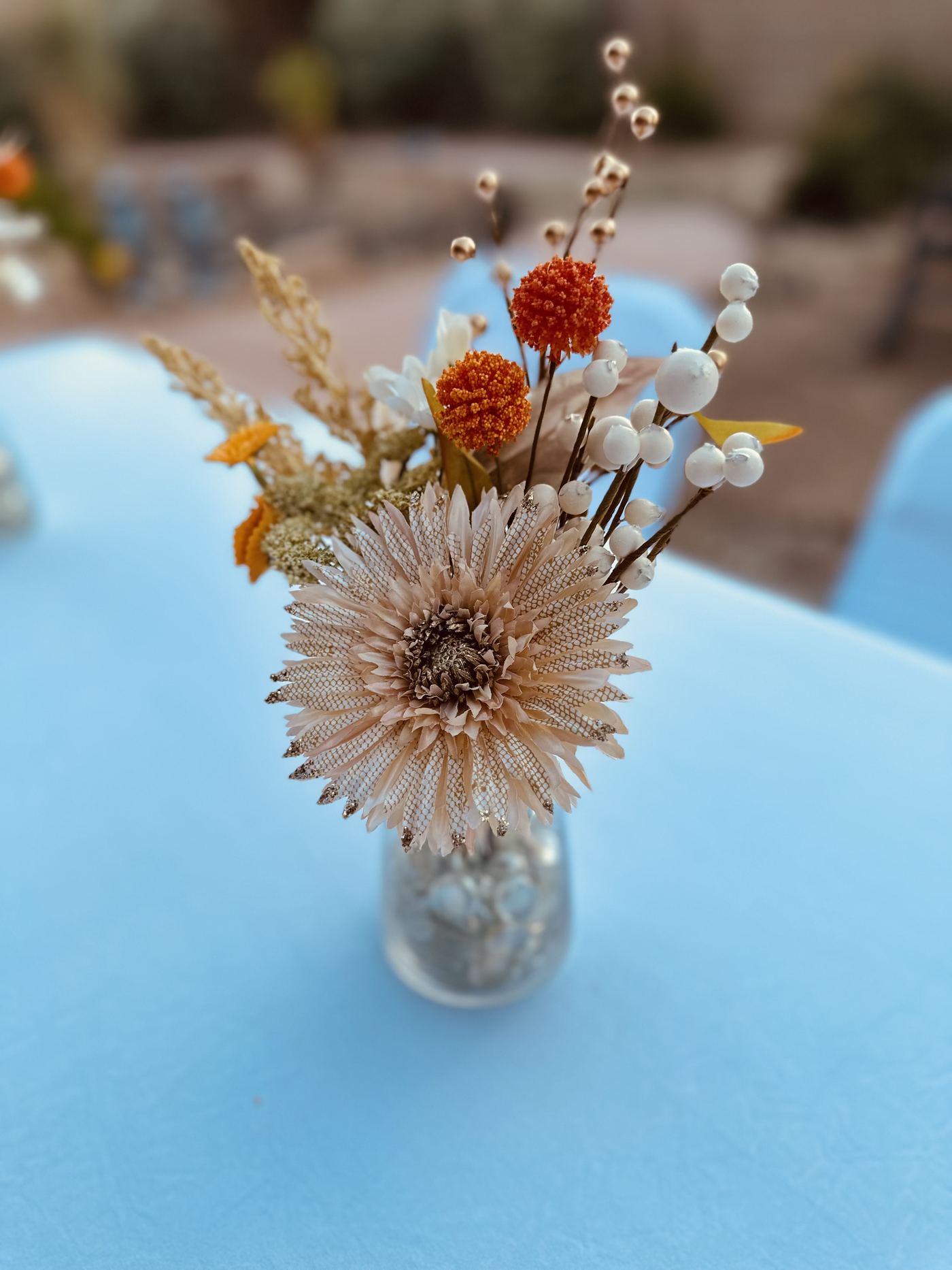Dried floral bud vase centerpiece on a white linen table at an outdoor event